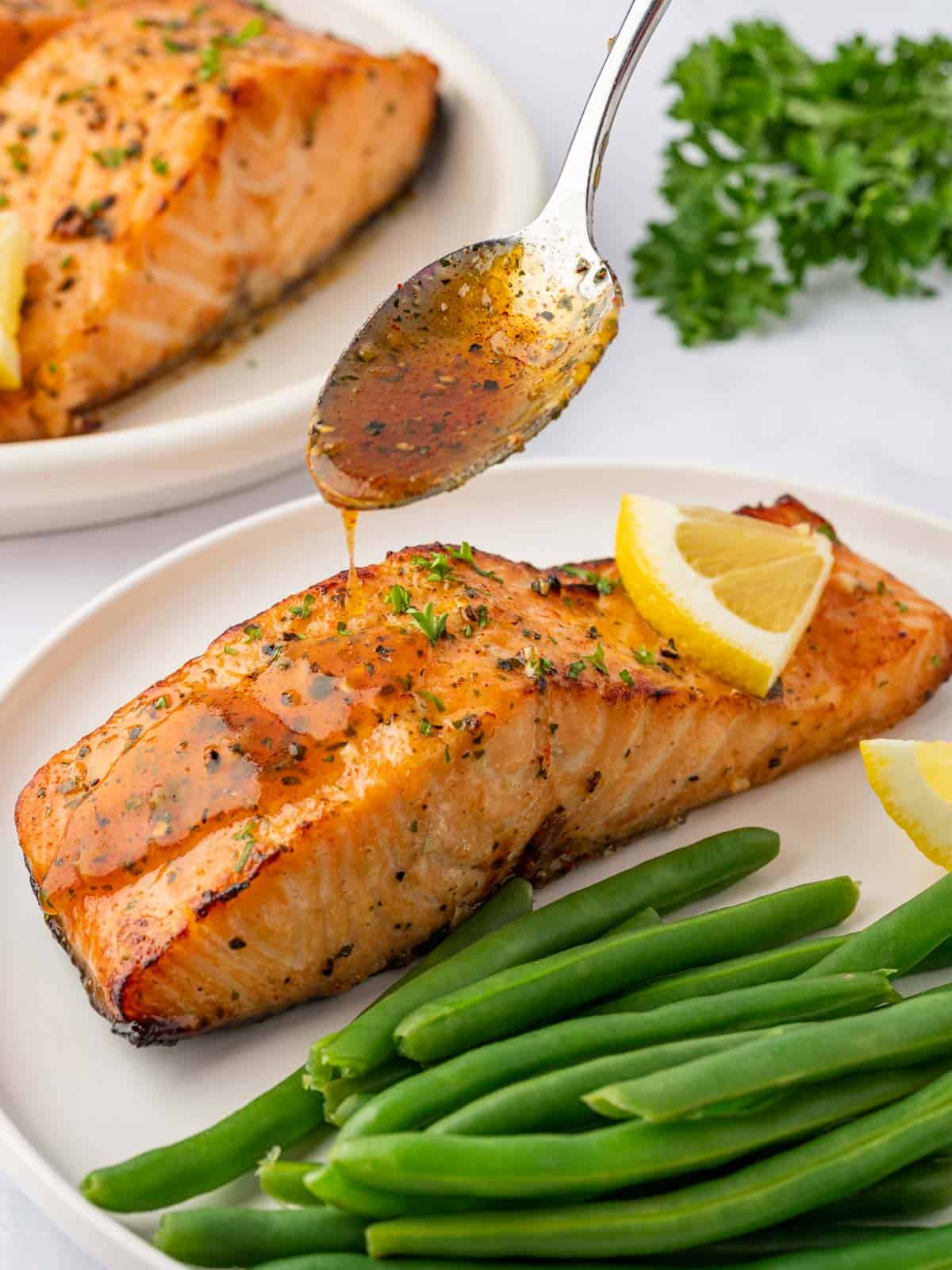 A spoon drizzles honey garlic sauce over a cooked salmon filet.
