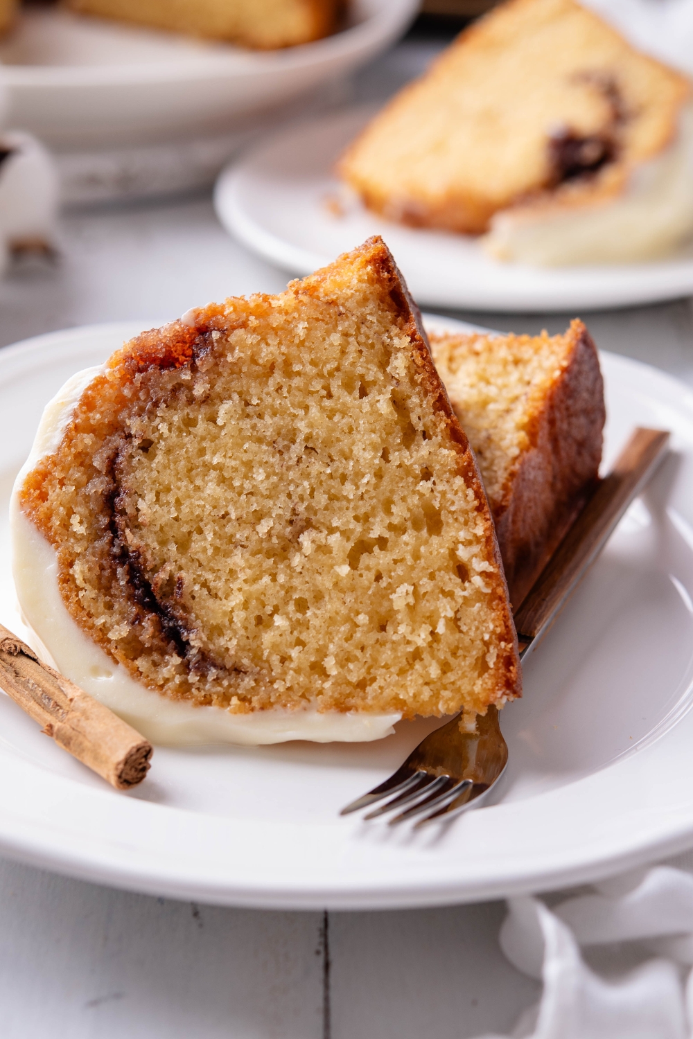 Two slices of cinnamon bundt cake are on a white plate. A fork rests on the plate as well.