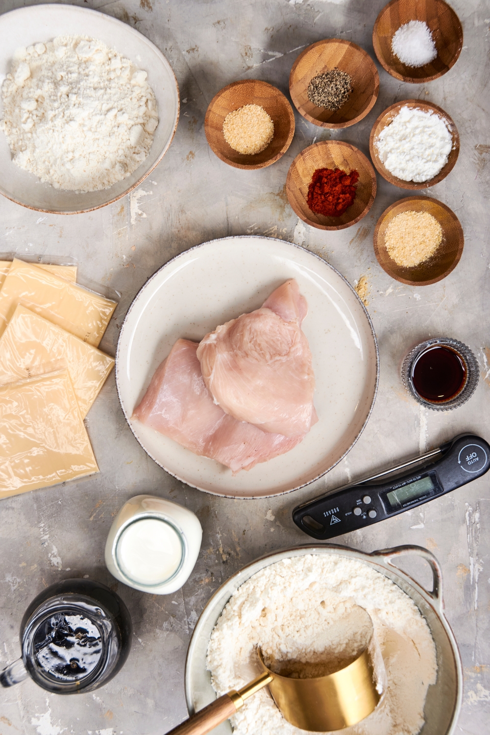 Chicken, seasonings, sliced cheese, flour, buttermilk, and maple syrup are all in separate containers on a gray counter top.