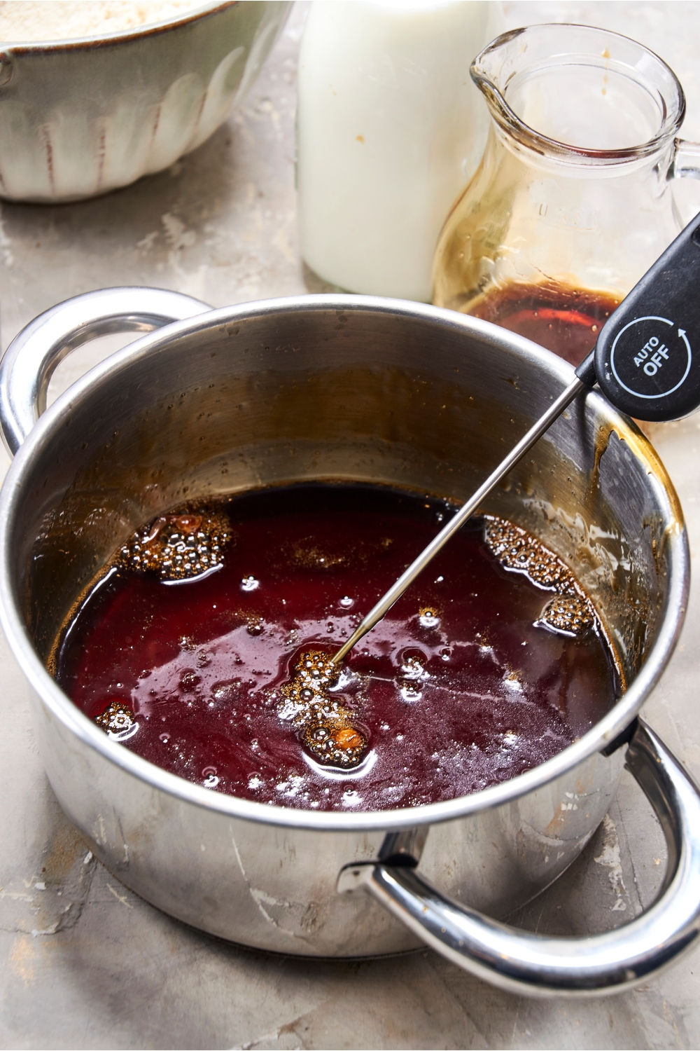 A meat thermometer rests in a pot of bubbling maple syrup.