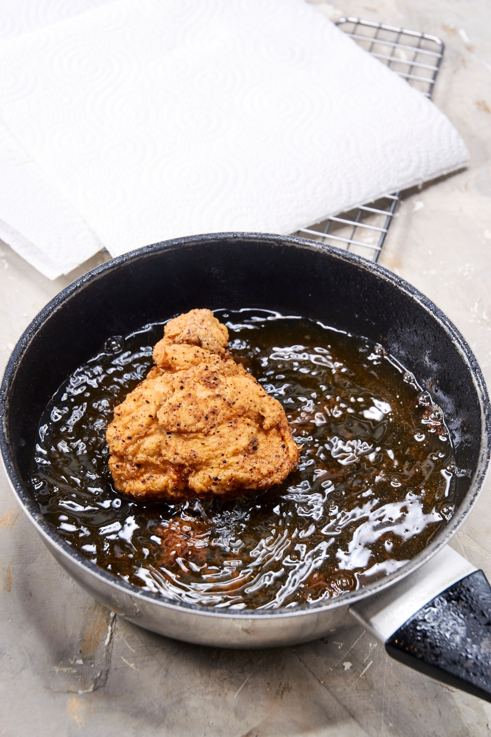 A golden piece of chicken is frying pan full of bubbling oil.